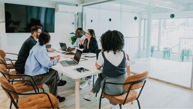 Cinq personnes travaillent sur des ordinateurs dans une salle vitrée